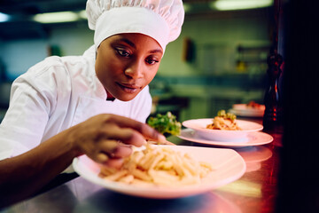Black female cook decorating  dish while serving food in restaurant. - obrazy, fototapety, plakaty