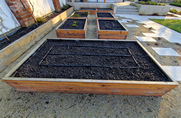 corner of the family garden with several beds bordered by boards. there is compacted sand around...