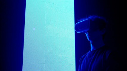 Man silhouette in virtual reality glasses standing in front of digital screen wall with neon...