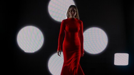 Female model against digital wall. Woman in red dress walking on runaway catwalk fashion show in...
