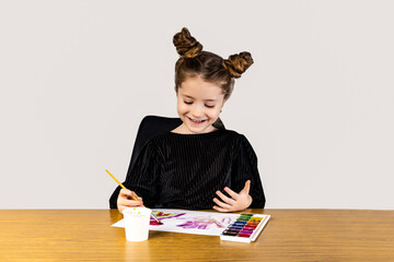 A little girl is smiling at a hardwood desk, painting with watercolors