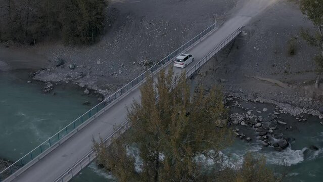 White automobile transportation movement over natural creek water stream with stones drone shot. Auto vehicle travel trip on concrete construction with speed flowing splash. Highway road transport 4k