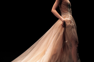 Fashion details of long evening beige chic lush dress on a female figure on a black background....