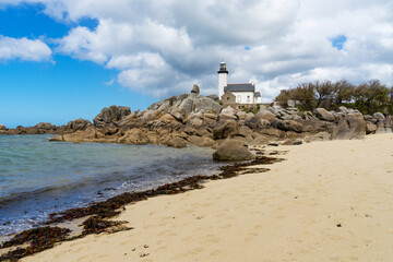 Sur la plage de sable jonchée de gros rochers, des algues marines marron ornent le rivage, tandis...