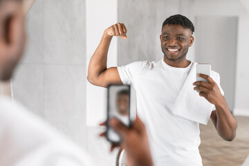 Happy young African man captures selfie showing biceps in bathroom