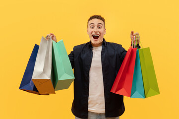 Excited young guy holding colorful paper bags purchases