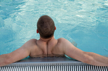 Man relaxing in swimming poll. Back view of anonymous shirtless man