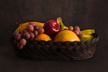 Still life of tropical fruits in a glass container. Includes grapes, apples, oranges, papaya, and bananas
