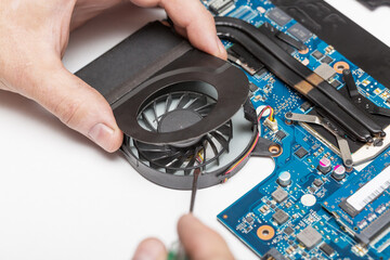 Computer service. Close up image of male technician engineer hand opening the laptop computer fan near the circuit board.