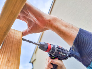 Worker using drill working on construction of wood frame house, gazebo