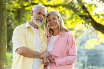 Smiling elderly couple holding hands, exuding happiness and love under the warm sunlight amidst lush greenery.