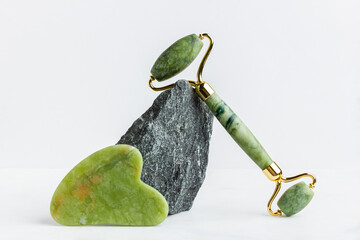 Green jade roller massager for face on white marble.