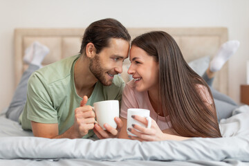 Cheerful couple with coffee, sharing moment in bed