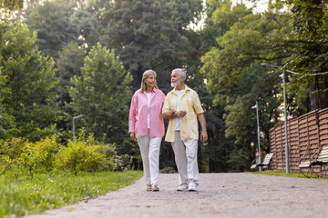 An elderly couple strolls hand in hand, exuding comfort and joy in a tranquil park, embodying lasting love and companionship.