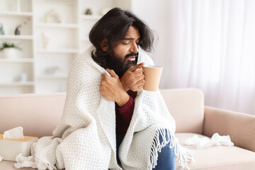 Sick millennial eastern man have cold or flu, drinking warm tea