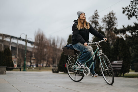 Casual young woman enjoying a peaceful bike ride in urban park setting.