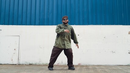 Hipster dancing b-boy foot step at street with blue wall. Asian break dancer practice street dance while stretch arms. Hip hop choreographer perform energetic dance. Outdoor sport 2024. Endeavor.