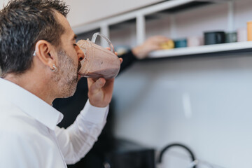 Taking a break in the office kitchen, the business person enjoys a protein shake.
