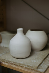 Fototapeta na wymiar Unfinished White Ceramic Vases on a Shelf Reflecting the Process of Pottery Making