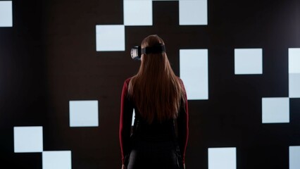 Person against big digital wall in studio. Woman in virtual reality glasses stands in front of...
