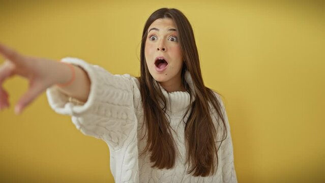 Simmering surprise! stunning young hispanic woman in yellow background, mouth agape in amazement, pointing ahead. isolated cutout of her great discover, wearing sweater, oblivious to the observer!