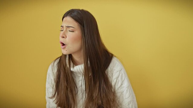 Furious young hispanic woman, beautiful in her anger, screams in frustration over isolated yellow background. enraged in her sweater, she stands fiercely before the cutout wall, her rage boiling over.