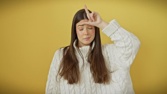Jovial young hispanic woman, exuding beauty in a snug sweater, throws a loser sign at folks, adding insult to injury while basking over an isolated yellow background