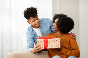 A delighted woman with a wide smile receives a polka-dotted gift box with a red bow from a man