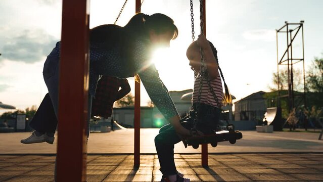 Caring young mother swinging on swing cute little daughter girl at sunny summer outdoor sport playground. Happy woman enjoy motherhood spending time with kid happy childhood leisure activity