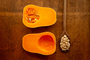 Two halves of sliced ripe butternut squash one with seeds and vintage wooden spoon on rustic wooden...
