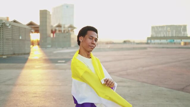 Portrait of a non-binary African American person waving the non-binary LGBTQ flag celebrating gay pride day. Lesbian, gay, bisexual, transgender social movements. Concept of happiness freedom love