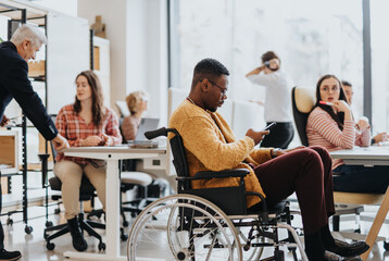 Handicapped male employee in wheelchair searching information on his phone while working together with his colleagues at modern office.