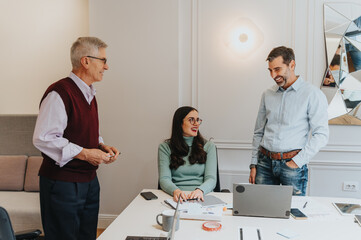 Two men and a woman enjoy a cheerful conversation in a bright office setting.