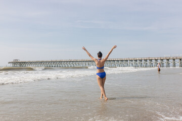 Woman in blue swimsuit running on the beach in Myrtle beach, South Carolina, USA. Summer background. 