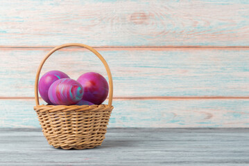 Colorful Easter Eggs in a Wicker Basket on Wooden Background - 747566274