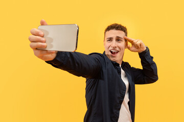 Charismatic young guy taking selfie on smartphone, yellow background