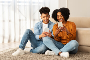 Smiling young African American couple sitting on a fluffy carpet, deeply engrossed in their...