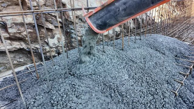 Concrete truck chute pouring wet cement mix into a foundation of a wall with rebar construction