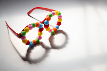 glasses adorned with small multicolored pompoms, illuminated by the sun with contrasts and beautiful shadows. Isolated and color space