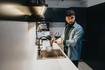 Man in the office kitchen enjoying a relaxed morning before work, preparing tea and happy to start the day while having a conversation with his coworker.