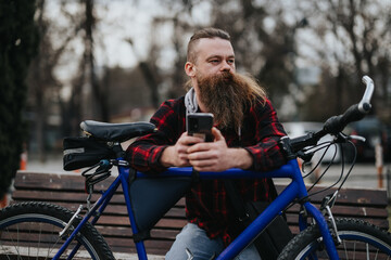 Fototapeta na wymiar Stylish bearded man with a smart phone relaxing on his blue bicycle at the park, showcasing an active lifestyle and modern connectivity.