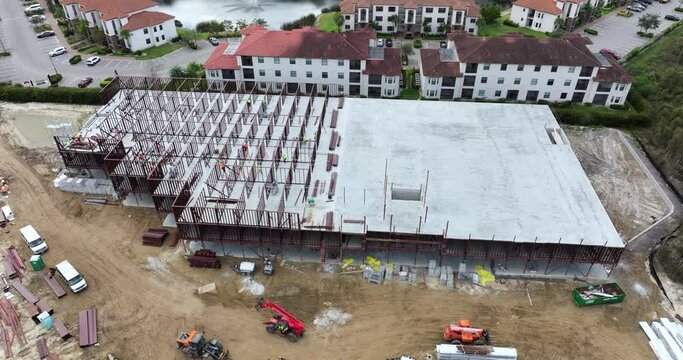 Development of commercial housing in USA. Construction works on monolithic frame. Large building site with scattered workers and equipment. Real estate market
