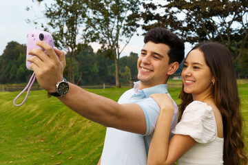 A young teenage couple taking selfie photos with an instant camera in a park