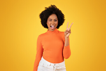 Vivacious young woman with fluffy afro hair winks and flashes a peace sign