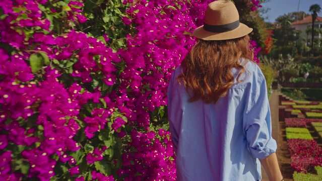 Traveler visiting a landmark garden with diverse vegetation of the island Madeira and Funchal city. Woman with hat and backpack walking between colorful flowers in botanical garden