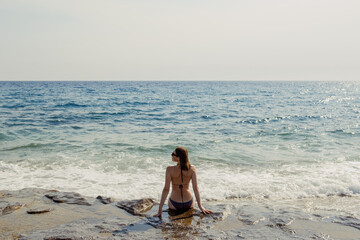 Fototapeta na wymiar A woman sits on a rock, looking out at the expansive blue sea, immersed in thought
