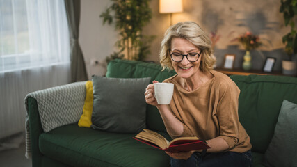 One woman mature caucasian female read book at home wear eyeglasses - obrazy, fototapety, plakaty