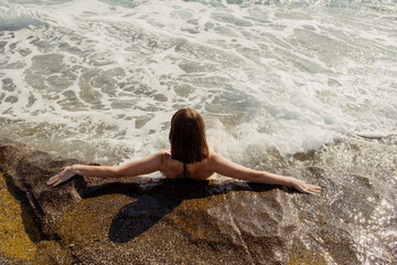 A person relaxes on a rock with arms outstretched, waves washing over in a soothing rhythm