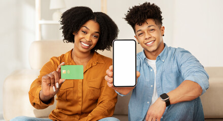 Cheerful couple showing a credit card and a smartphone with a blank screen