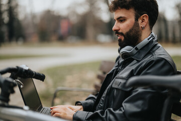 Stylish male entrepreneur manages tasks on his laptop while sitting outdoors in an urban park, with his bicycle nearby, epitomizing modern remote work.